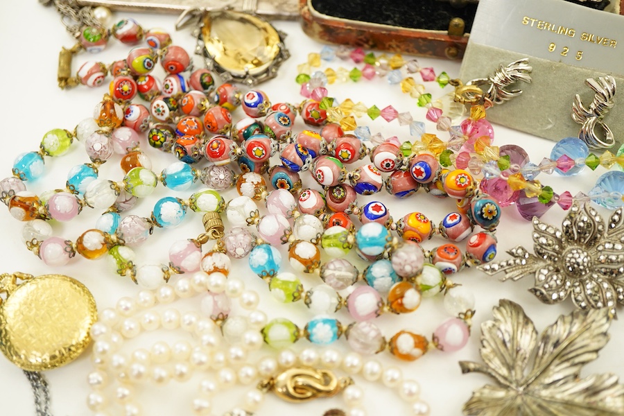 A collection of costume jewels, comprising: a charm bracelet suspending a series of charms, some in silver; a silver pencil; a sycamore leaf brooch; a pair of earrings of knotted design; an Art Deco paste watch; a gilt m